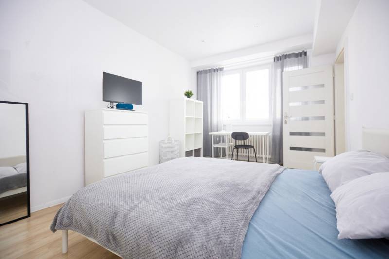 Bright bedroom with a bed, mirror, dresser, and wood-patterned floor.