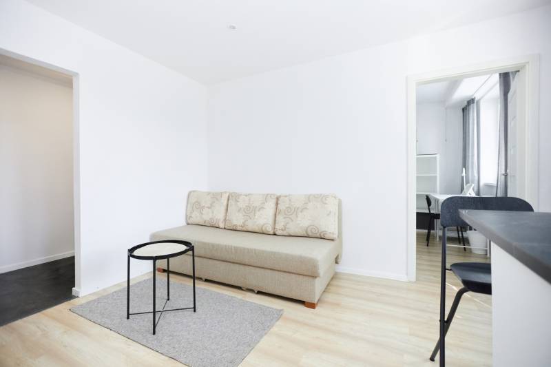 Living area with a sofa, table, and wood-patterned flooring in a two-room apartment.