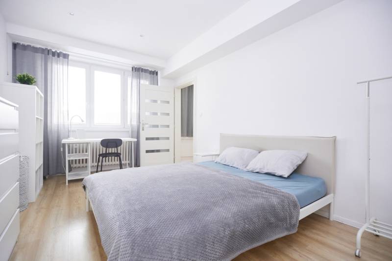 Bright bedroom in a two-room apartment with a desk and wood-decorated flooring.