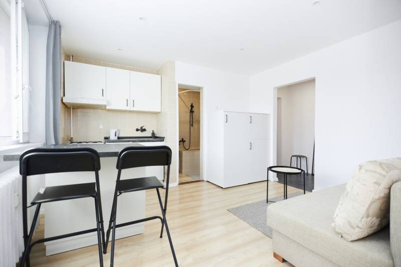 Interior of a 2-room apartment with a kitchen, bar stools, and a wooden decor floor.