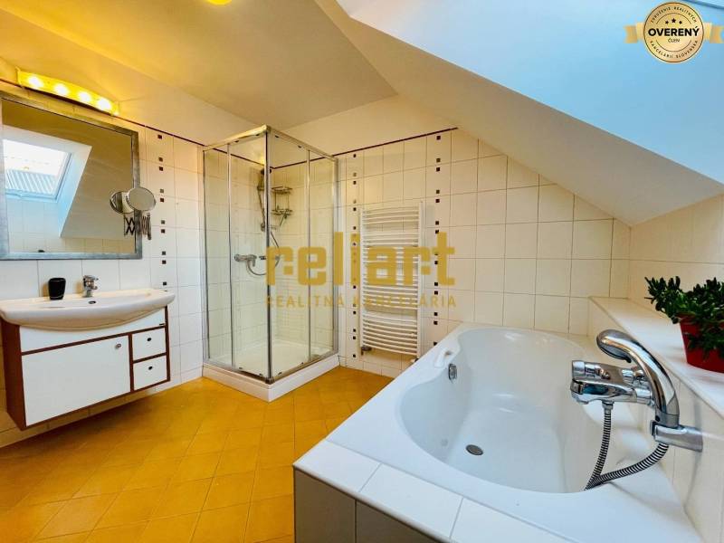 A bathroom in a family house with a bathtub, shower corner, and slanted ceiling.