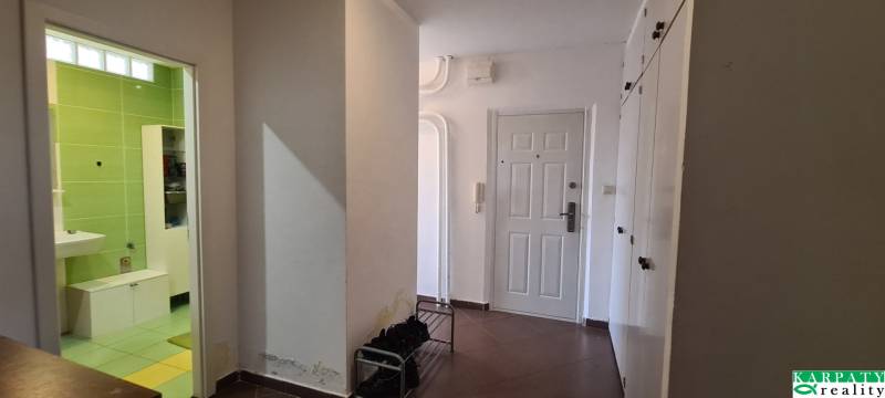 A hallway in a 3-room apartment with white walls and brown tiles.