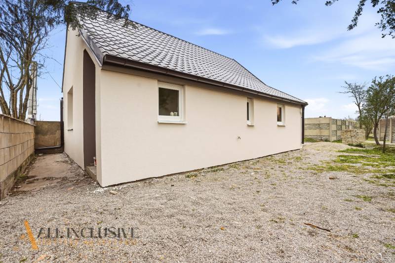 A family house in Dolný Bar with a white facade and a sloped roof on a rocky plot.