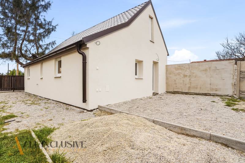 A family house in Dolný Bar with a white facade and a sloped roof on a gravel plot.