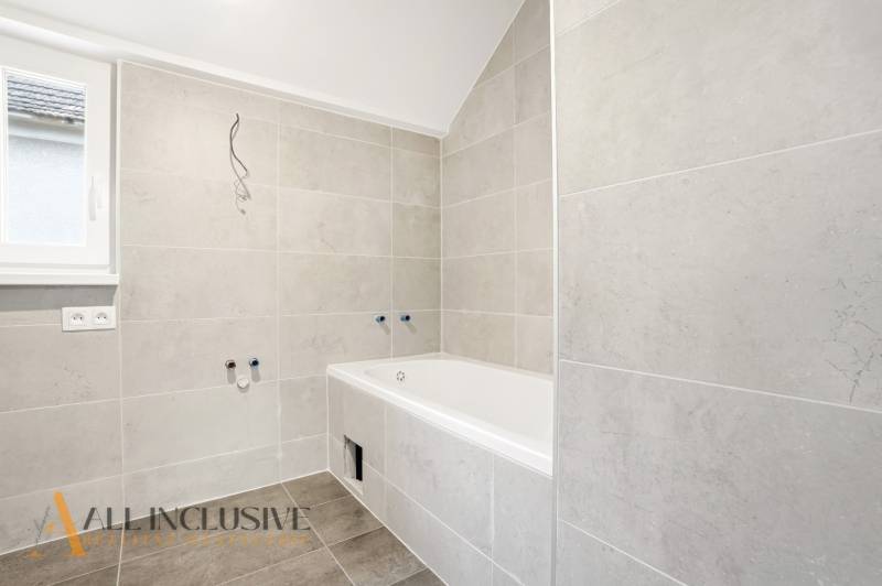 A bathroom in a family house with a bathtub and light tiles on the walls.