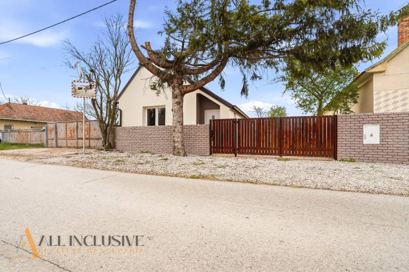 A family house in Dolný Bar with a wall and a gate, surrounded by trees and cement.