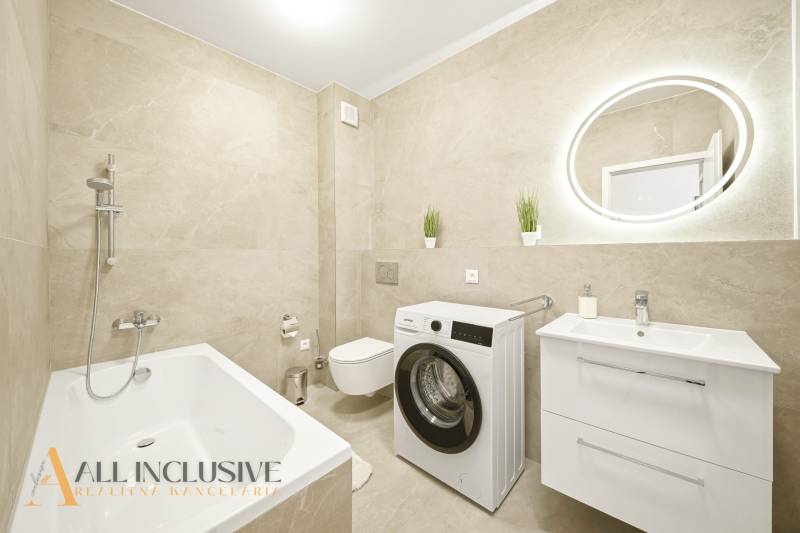 Bathroom with shower, washing machine, and sink in a 4-room apartment with beige tiles.