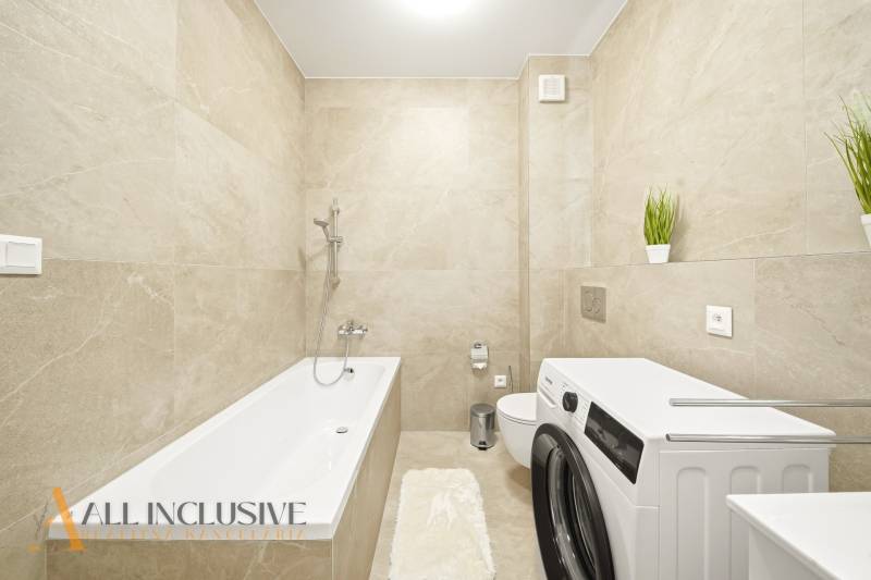 A bathroom with light tiles, a bathtub, a washing machine, and decorative plants in a 4-room apartment.