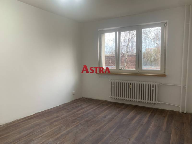 A room with white walls, a wooden decor floor, and a large window in a 2-room apartment.