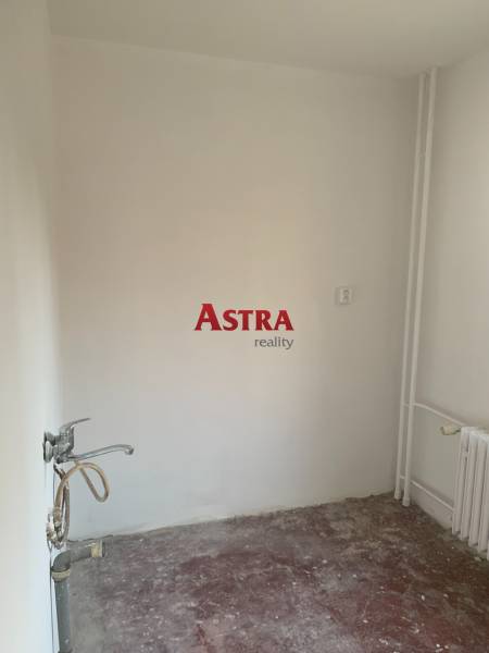 An empty room in a two-room apartment without flooring and with a sink.