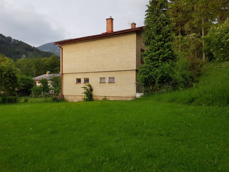 A family house in Blatnica on Blatnica Street surrounded by greenery and trees, with mountains in the background.