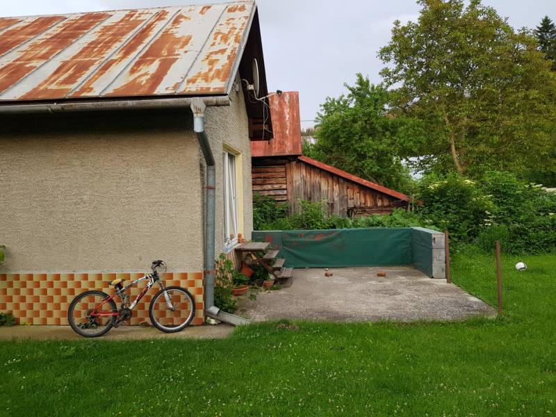 A family house in Blatnica with a garden, a bicycle leaning against the wall, a visible wooden shelter.
