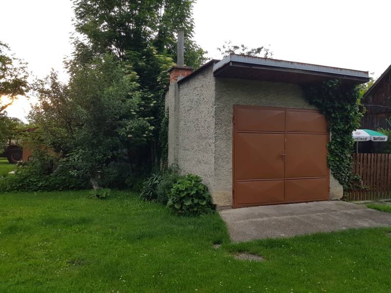 A garage in a family house on a street in Blatnica, surrounded by greenery and climbing plants.