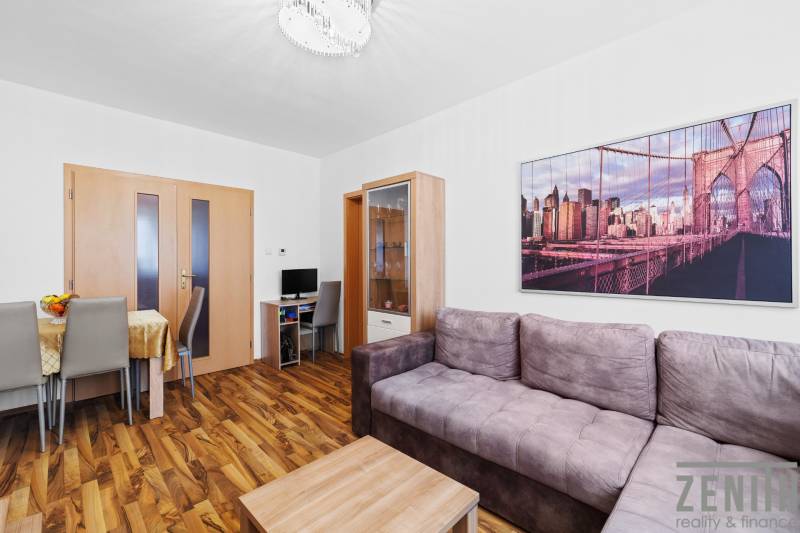 Living area of a 2-room apartment with a sofa and wooden decor flooring.