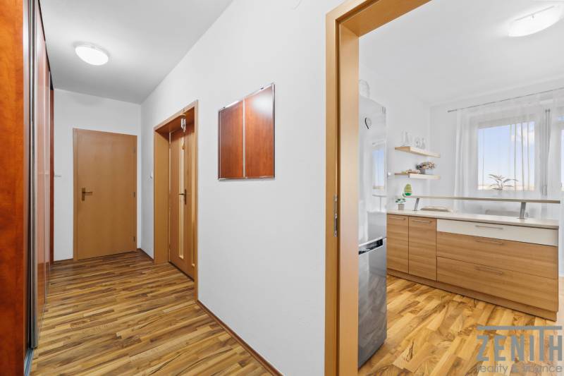 A hallway in a 2-room apartment with a wooden decor floor and a view into the kitchen.