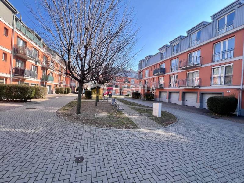 Apartment complex with orange facades, trees, and landscaped walkways. Suitable for a one-bedroom apartment.