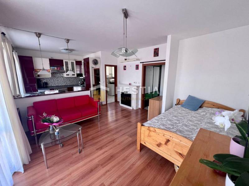 Living room with a red sofa, glass table, and kitchen in a studio apartment.