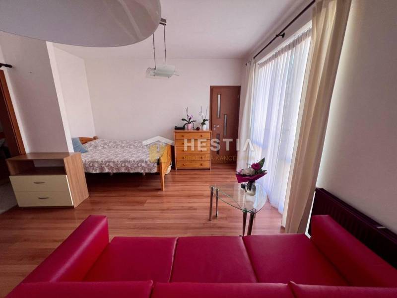 In the photograph is a studio apartment, including a bed, a red sofa, and a glass table.