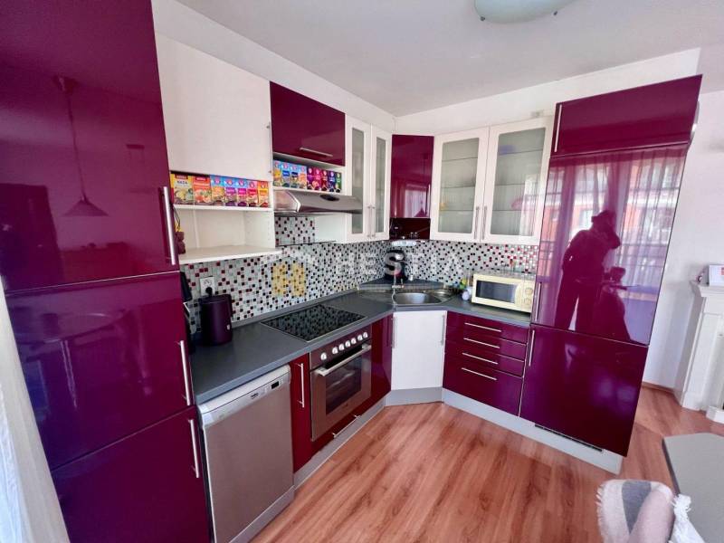A kitchen in a studio apartment with glossy cabinets and mosaic on the wall.