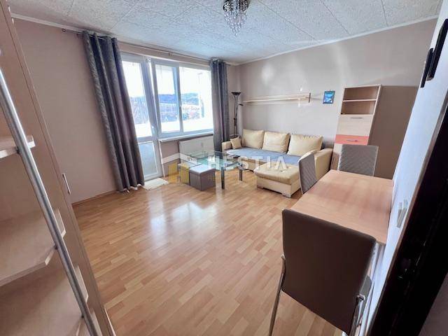 Living room of a two-room apartment with a wooden decor floor and light furniture.