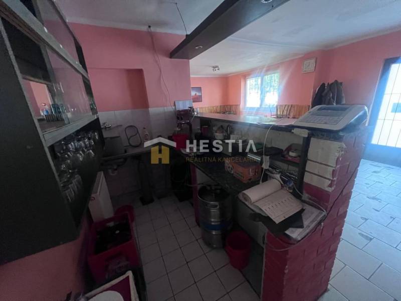 Interior of a gastro space with a bar counter, cash register, and glasses on a shelf.