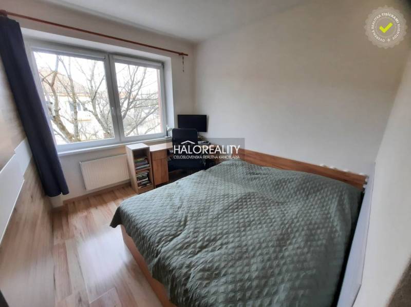 A bedroom in a three-room apartment with a wood-patterned floor and a large window.