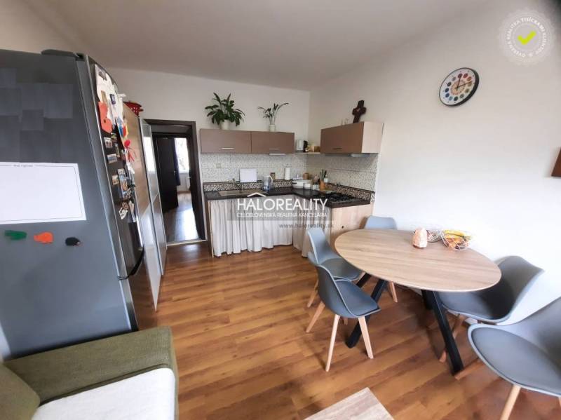 A kitchen of a three-room apartment with a wooden decor floor, a dining table, and appliances.