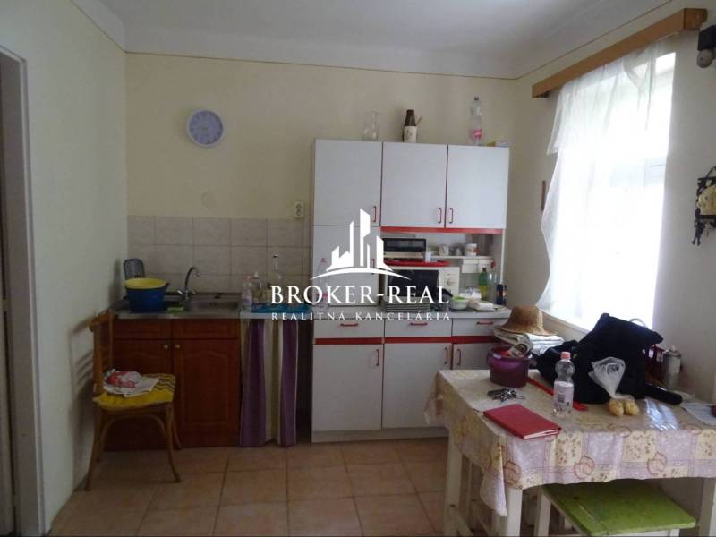 A kitchen in a family house with white furniture and a table with a plastic tablecloth.