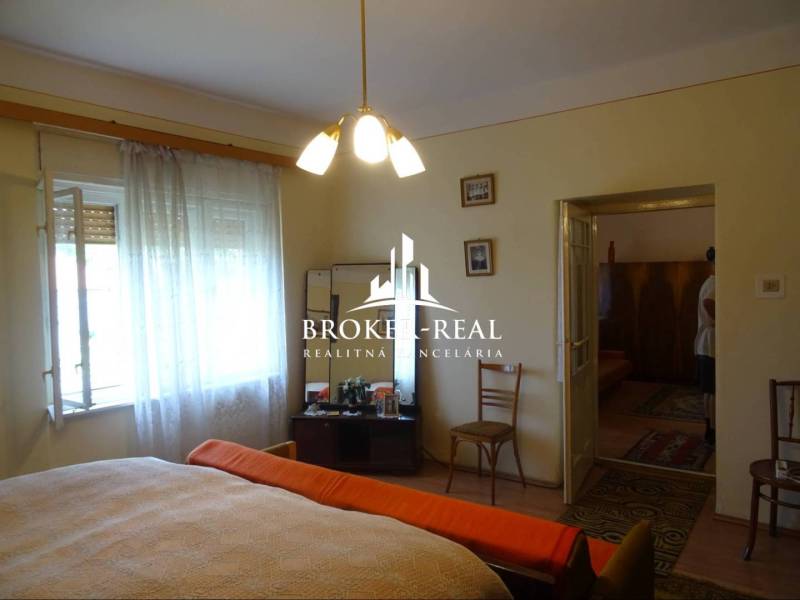 Bedroom in a family house with a wooden decor floor, bed, armchair, chairs.