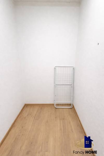 A white room in a two-room apartment with a wood-patterned floor and a drying rack.