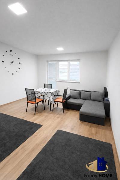 Living room in a two-room apartment with a sofa, table, and wooden decor flooring.