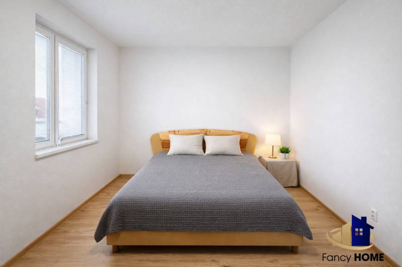 A bright bedroom with wood-patterned flooring in a 2-room apartment, decorated with a bed and a lamp.