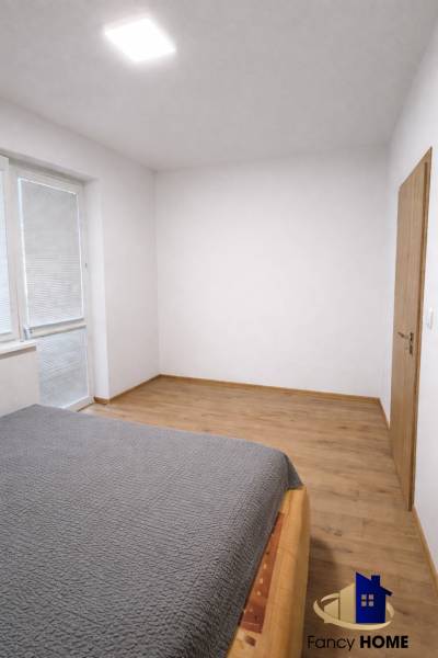 A bedroom in a two-room apartment with a wooden decor floor and a large window.