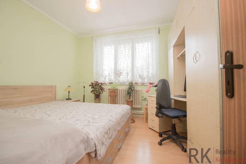 A bedroom in a family house with a wood-patterned floor, a bed, and a desk.