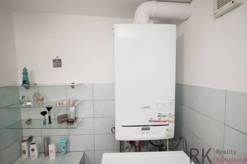 A bathroom with a gas boiler and shelves for cosmetics in a family house.