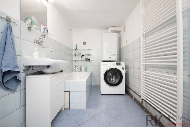 A bathroom in a family house with a bathtub, sink, washing machine, and ladder radiator.
