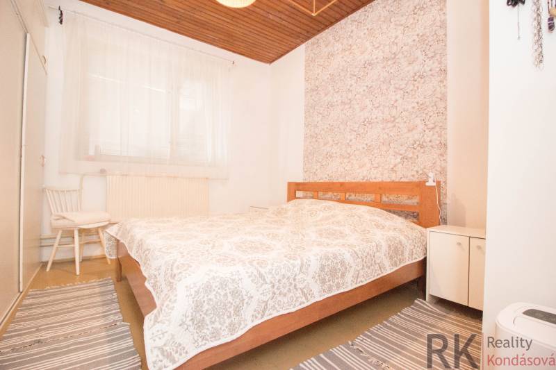 A bedroom in a family house with a wooden ceiling, decorative wallpaper, and striped carpets.