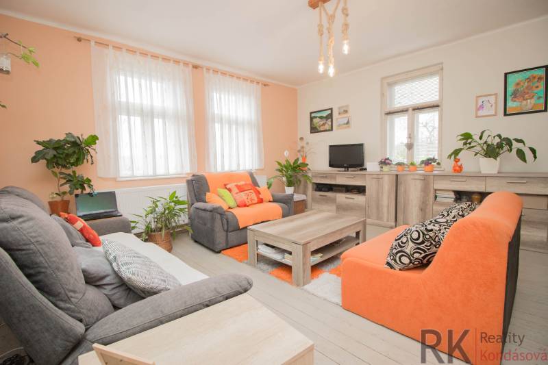 A living room in a family house with orange sofas, plants, and a wooden decor floor.
