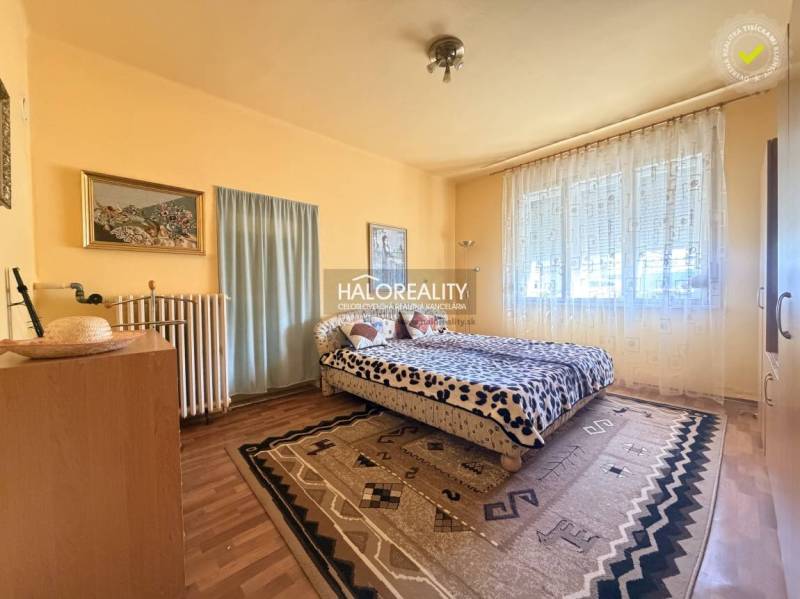 Bedroom in a family house with wood-patterned flooring, a large window, and carpets.
