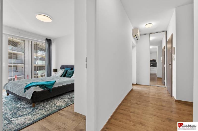A bedroom with a large window and a hallway with a wooden decor floor in a 2-room apartment.