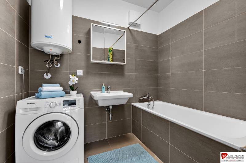 A bathroom in a 2-room apartment with a washing machine, bathtub, sink, and gas boiler.