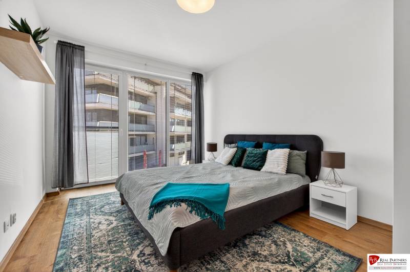 A bedroom with a large bed, balcony doors, and a wooden decor floor in a 2-room apartment.
