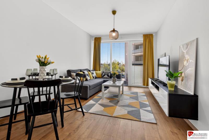 Living room in a two-room apartment with a wooden decor floor, a sofa, and a dining table.