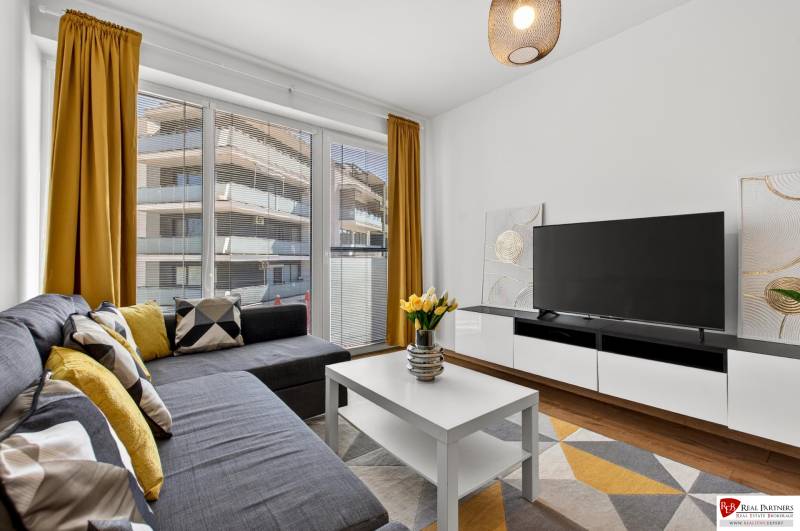 A two-room apartment with large windows, a sofa, a television, yellow curtains, and a wooden decor floor.