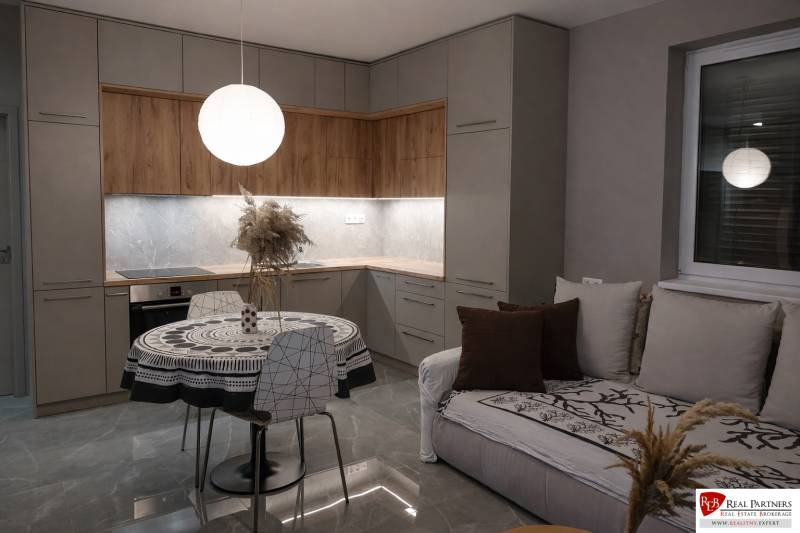 A kitchen in a 2-room apartment with a wooden decor floor and a round table.