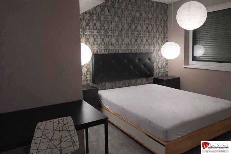 Bedroom with a bed, evening lighting, table, and chair in a two-room apartment.