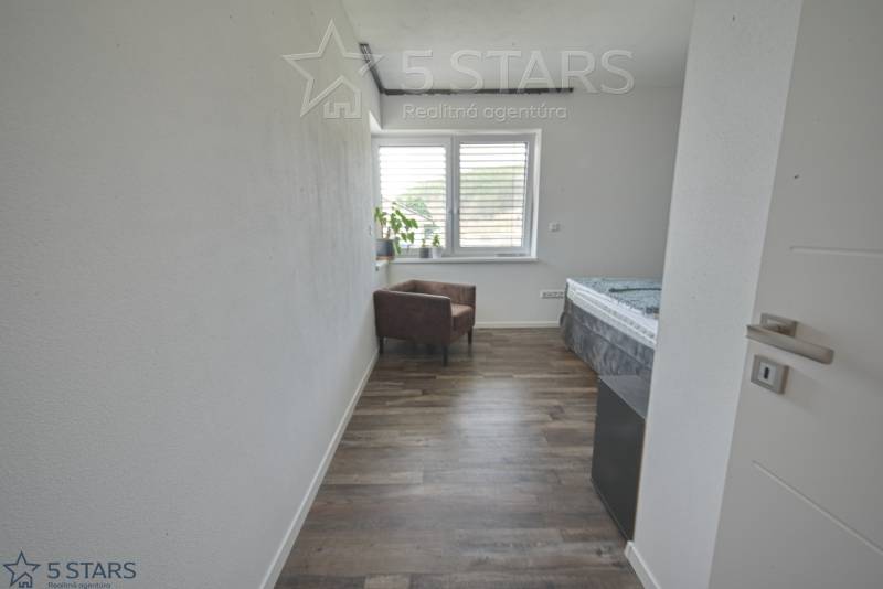 A room in a family house with a floor with a wooden decor, an armchair, and a window.