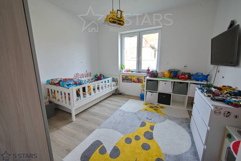 Children's room with a bed, toys, a giraffe-themed rug, and a wooden decor floor.