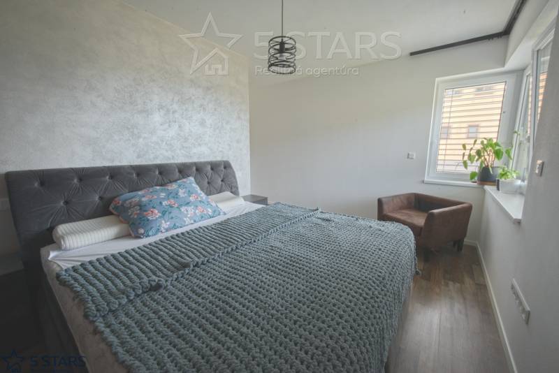 A bedroom in a family house with a bed with a textile headboard and a floor with a wooden decor.