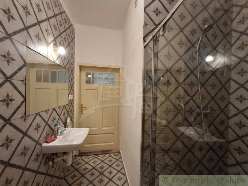 Bathroom with a tiled wall, mirror, sink, and shower in a family house.
